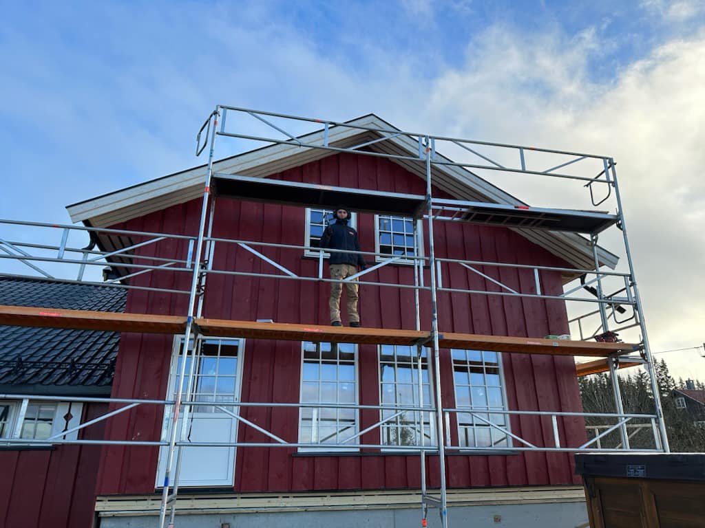 Tømrer fra Olastuen Bygg AS monterer stillas på en rød bygning i Våler