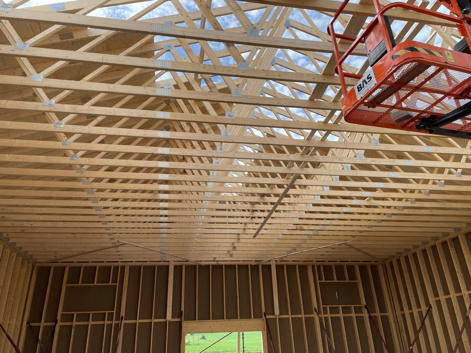 Innvendig visning av takverk i tre under oppføring, med synlige sperrer og sakseløft i byggegrop
